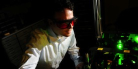 Dr. Jennewein wearing red protective glasses looking at an optics table